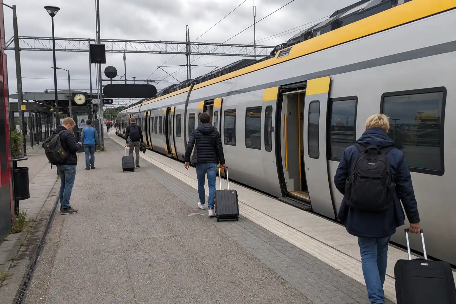 Resenärer med resväskor kliver på ett regionaltåg vid en perrong under tågresor en mulen eftermiddag